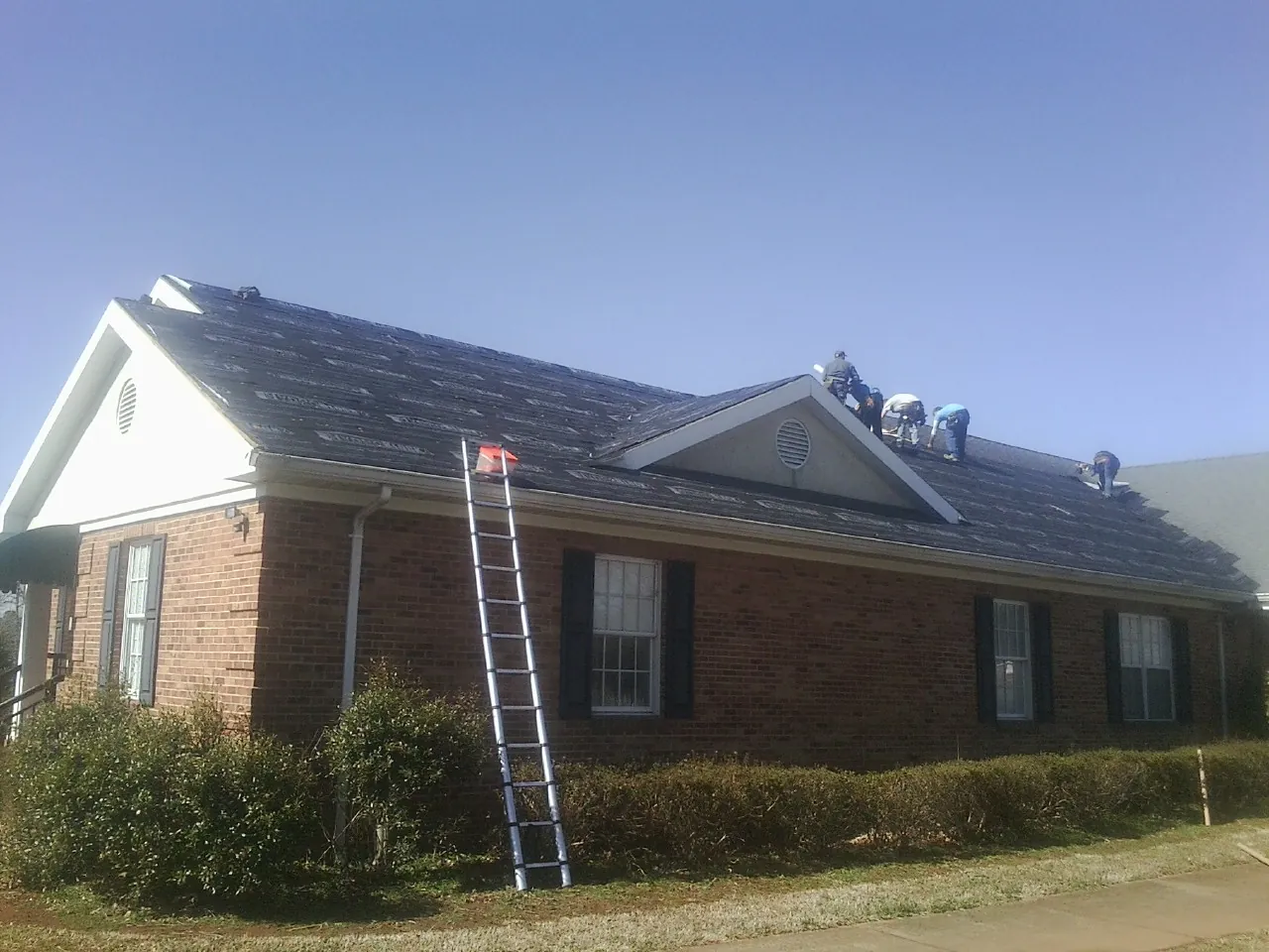 Crew tearing shingles off a brick ranch roof with a ladder set — Metal Roof Repair work by our crew in Woodland